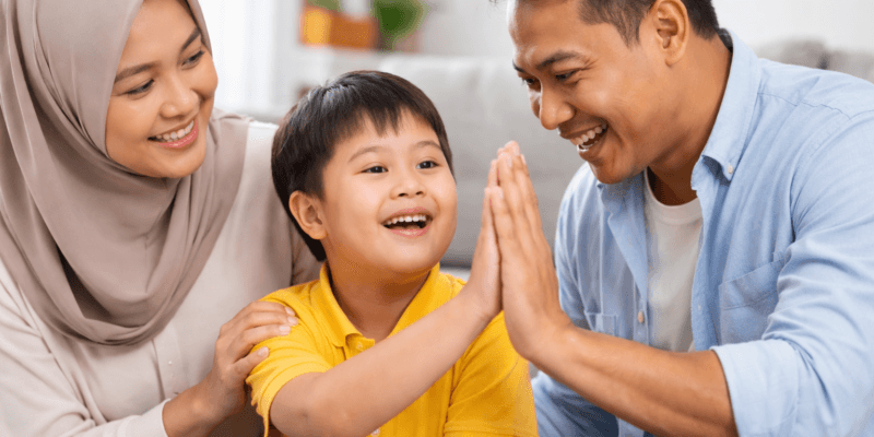 Anak berkebutuhan khusus wajah Jawa Indonesia sedang berinteraksi hangat dengan kedua orang tuanya di ruang tamu rumah yang nyaman dan terang.