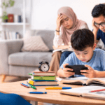 Anak bermain gadget di meja belajar sementara orang tua terlihat khawatir karena dampak kecanduan gadget pada anak