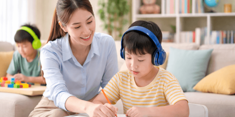 Guru privat membantu anak berkebutuhan khusus belajar menulis di rumah dengan suasana ruang tamu yang nyaman dan tenang.